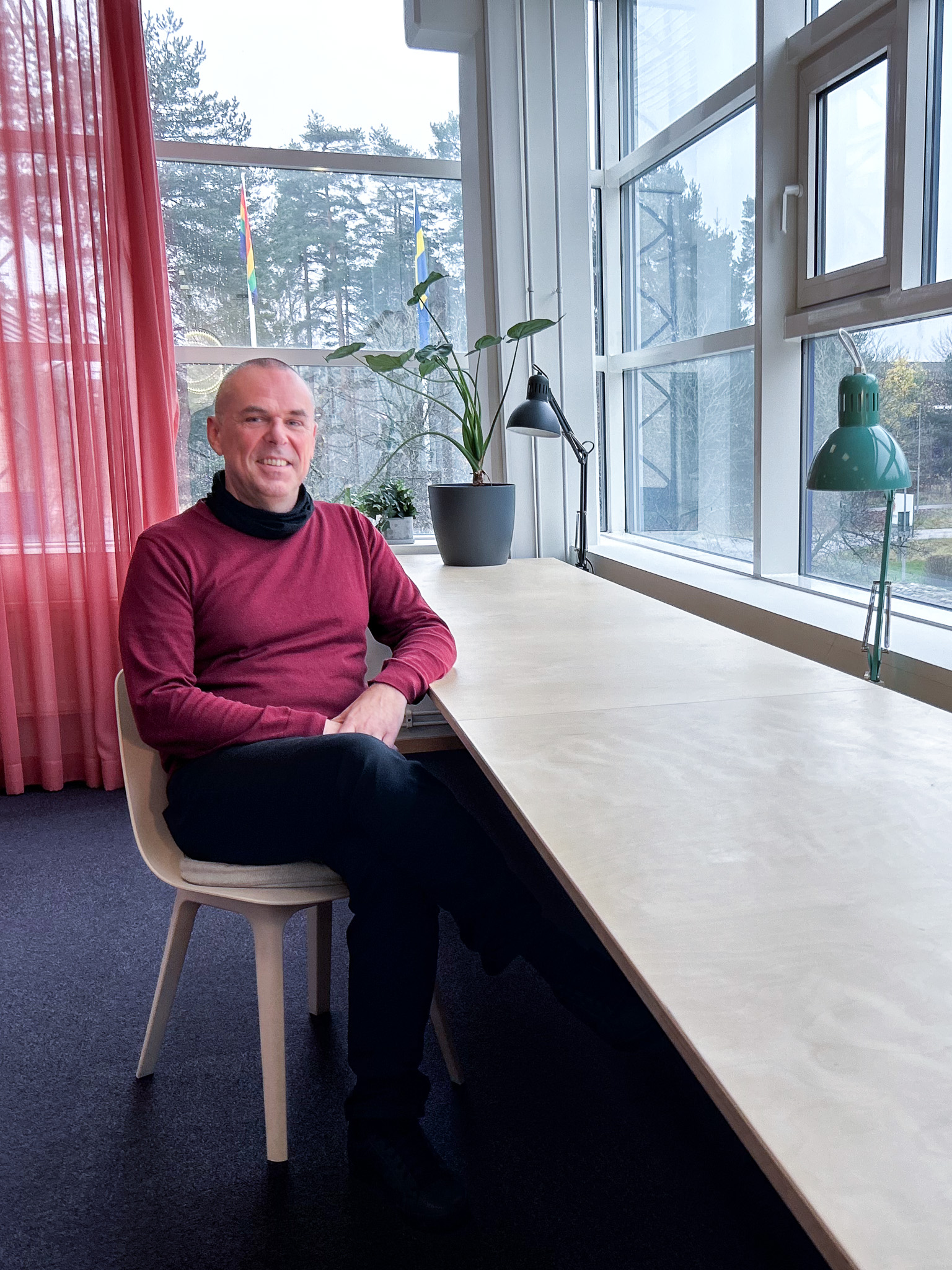 Man i röd tröja som sitter på en stol vid ett bord.